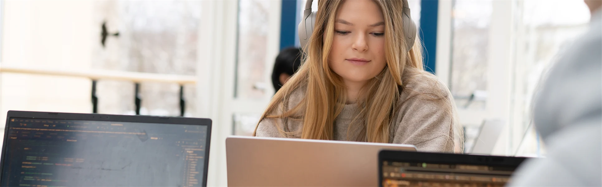 En kvinna med hörlurar sitter vid en laptop