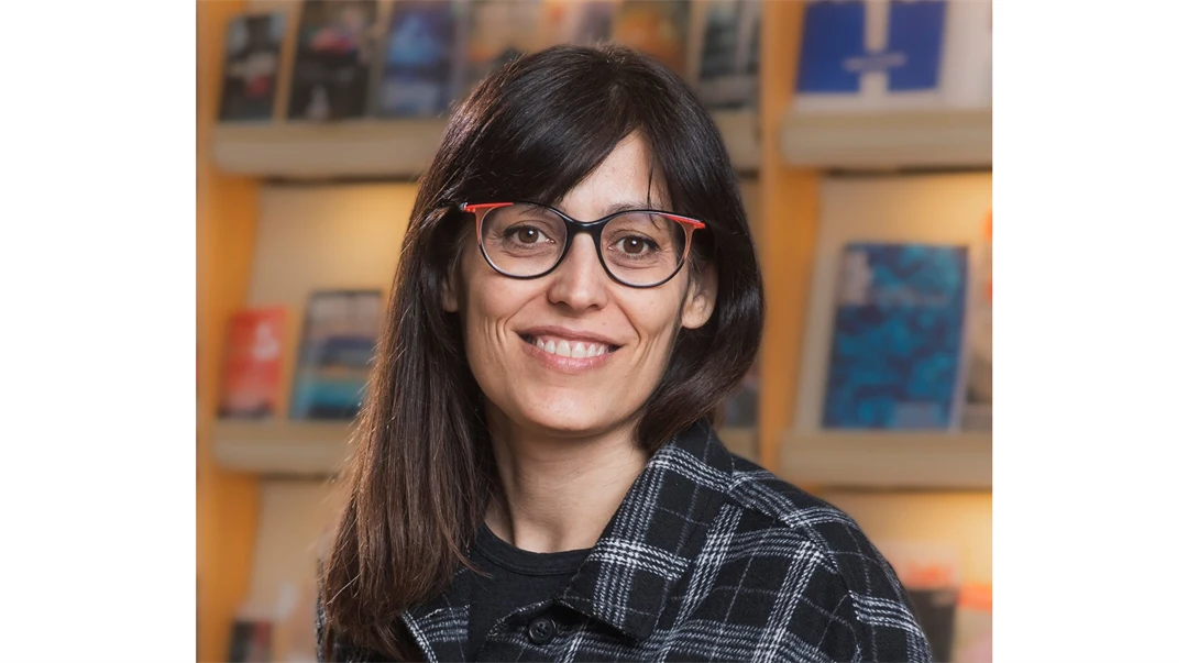 A woman with dark long hair, glasses and wearing a plaid shirt.