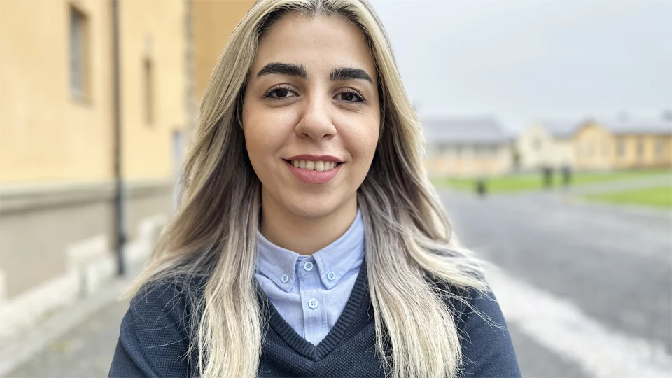 Leende kvinna framför gul byggnad.