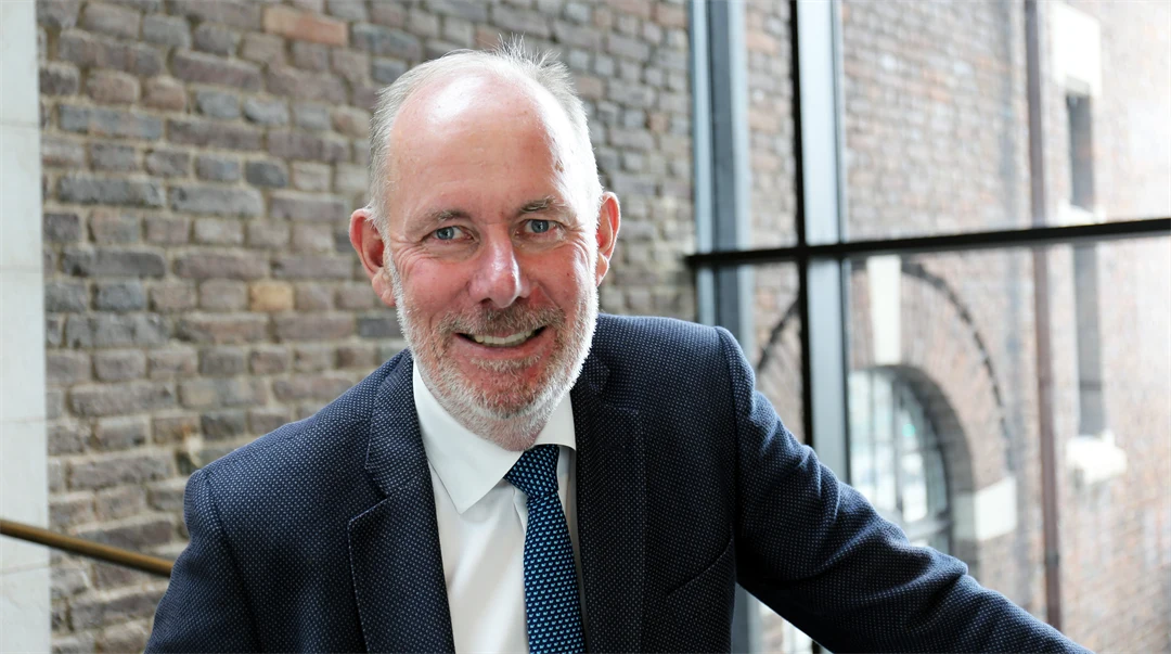 Man in dark blue jacket, white shirt and tie smiles and looks at the camera.