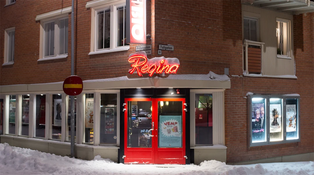 Skyltfönstret och entren till en liten biograf i Östersund. Den har röd entredörr och ovanför dörren sitter en neonskylt som visar biografens namn Bio Regina