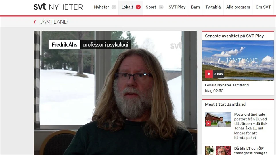 Skärmklipp från nyhetssida med en bild av en skäggig man framför ett fönster.
