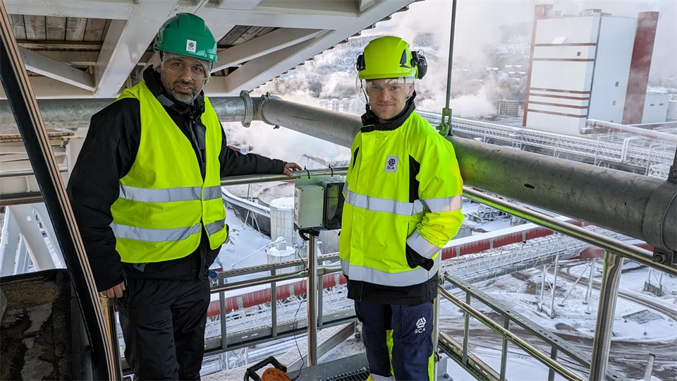Two men in warning clothes in a wintry industrial landscape.