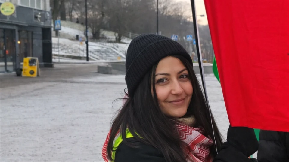 Foto av en kvinna som står utomhus vid ett rött tygstycke.
