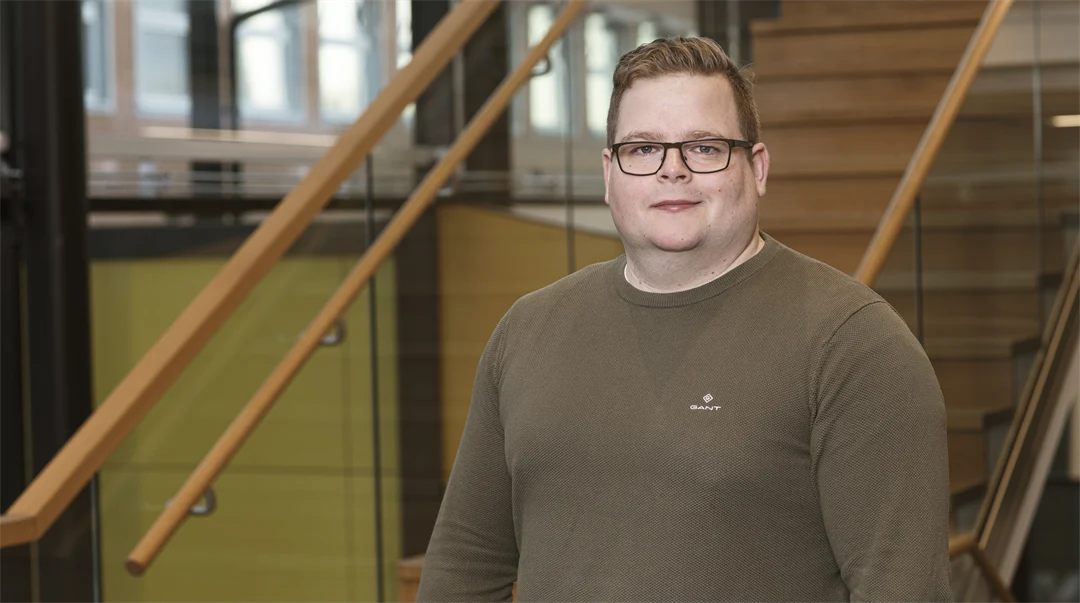 En man med glasögon och brun tröja ler mot kameran