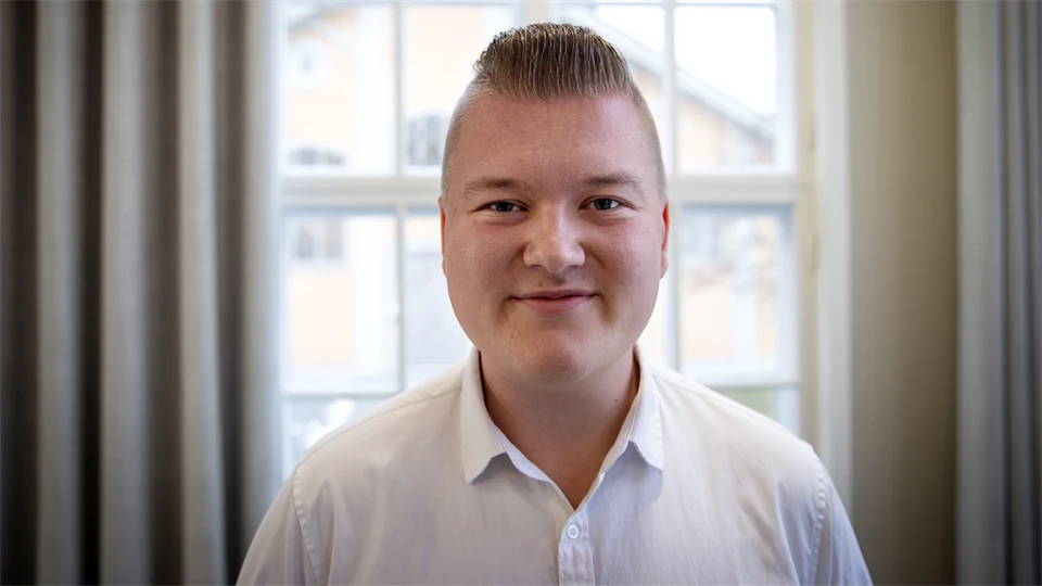 Man med vit skjorta och kort hår står vid fönster.