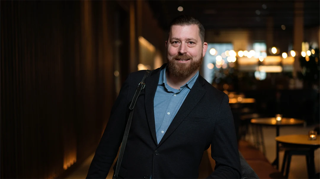 En man står i ett mörkt rum med några mindre bord i bakgrunden.