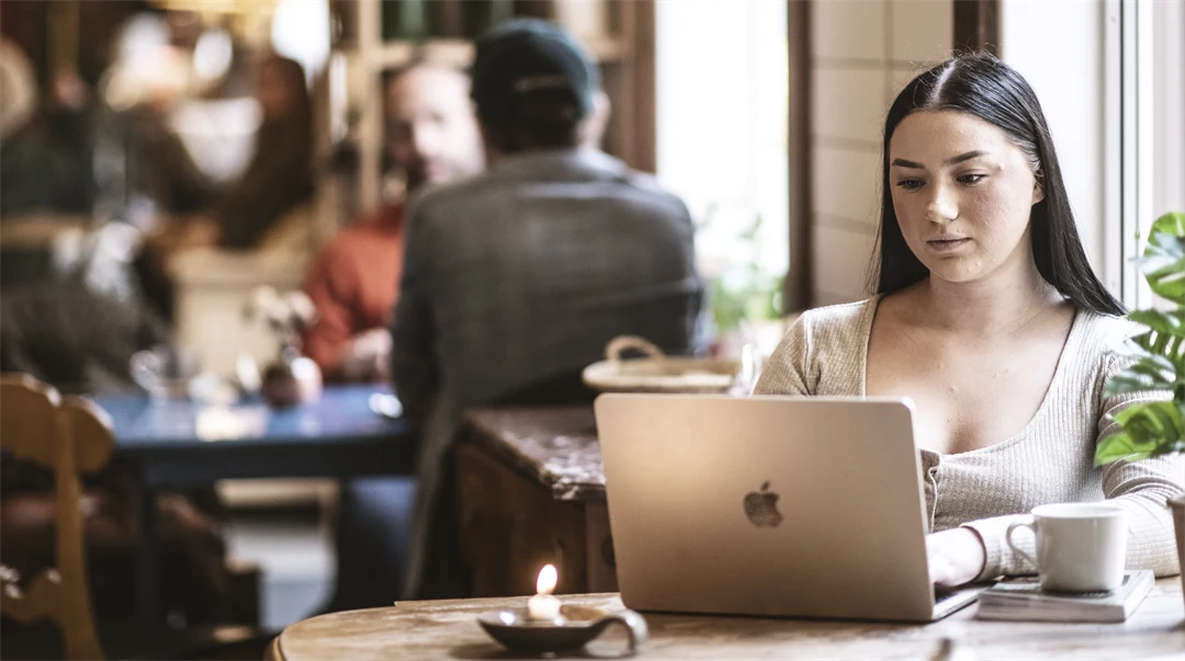 En kvinna sitter på ett kafé och jobbar vid sin dator. 