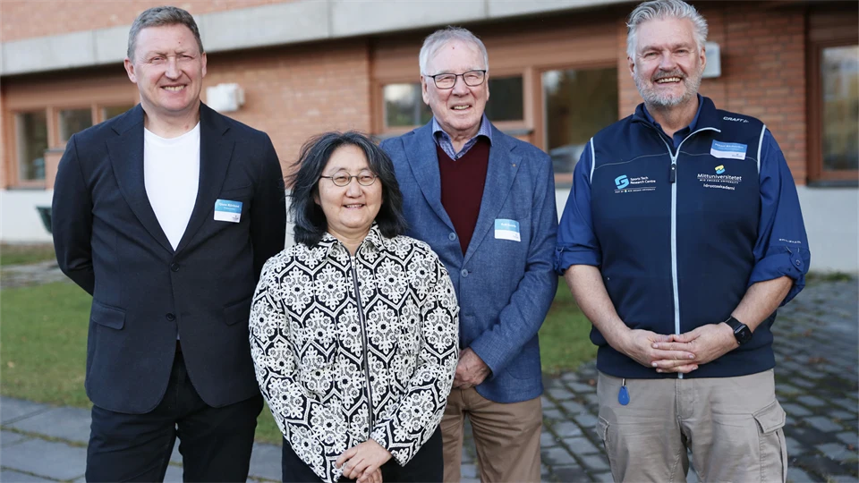 Gruppbild med leende personer framför tegelbyggnad