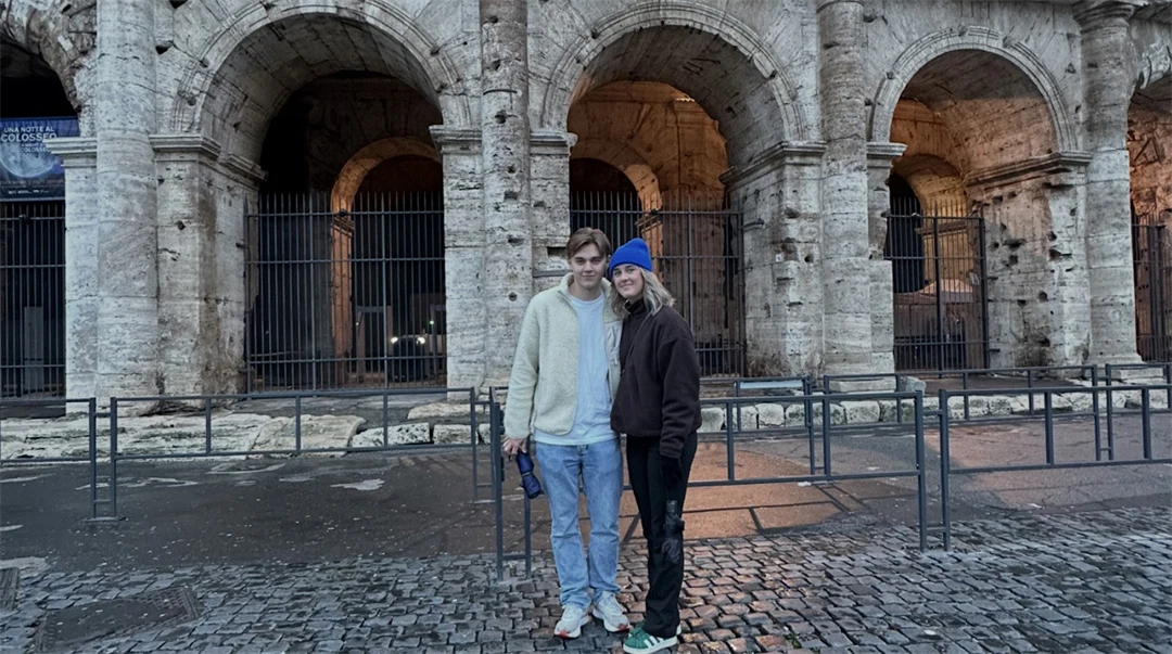 Två personer står framför en stenbyggnad med välvda ingångar.