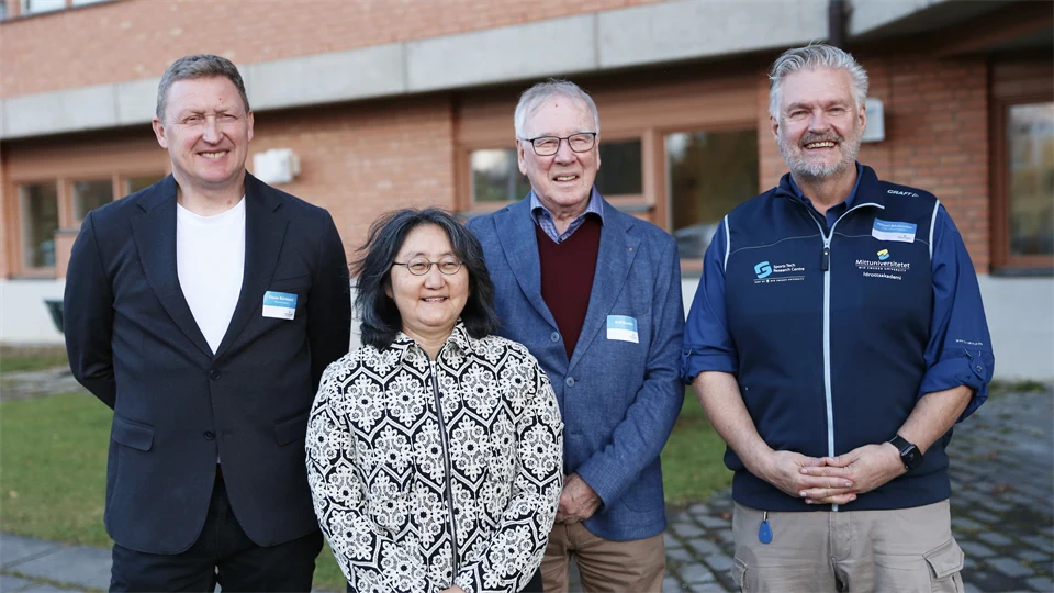 Gruppbild med leende personer framför tegelbyggnad
