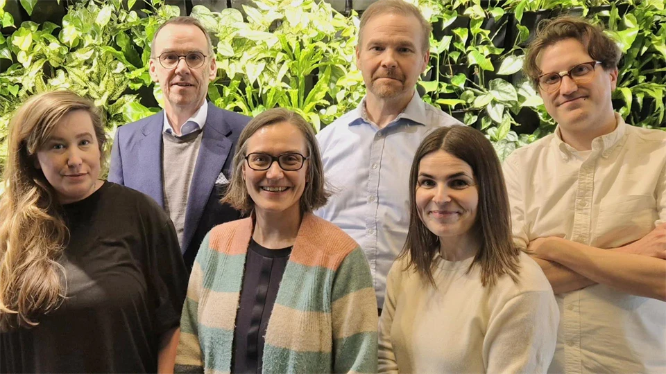 Tre män och tre kvinnor står i grupp framför gröna buskar.