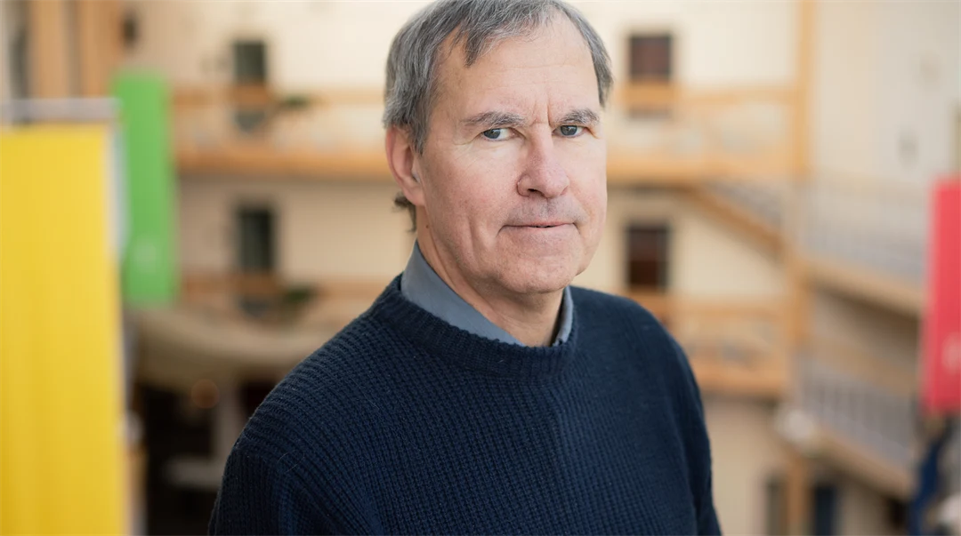 En man med grått hår, mörkblå tröja och mörkgrå skjorta. 