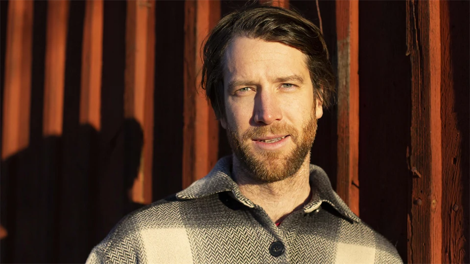 Portrait of a man outdoors with red panel wall in the background.