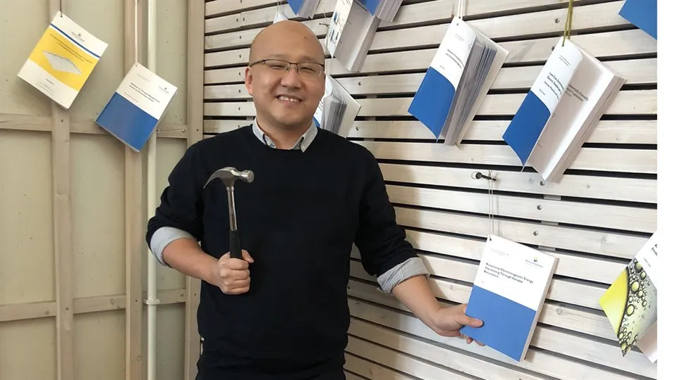 Ye Xu holding a hammer and his thesis that is nailed to the wall.