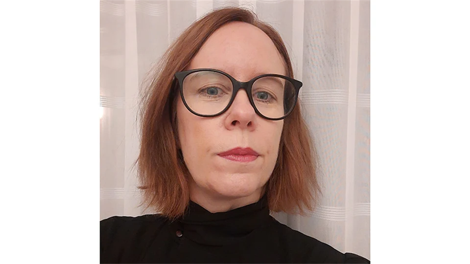 Kvinna med svarta glasögon, rödlätt hår och klädd i en svart tröja.