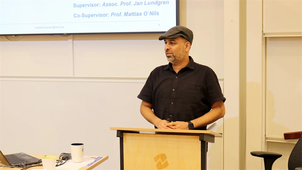 Man i svart skjorta och grå keps står och håller en presentation.
