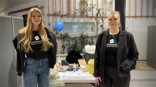 Två personer med mörka kläder och ljust hår står framför ett bord med provtagningsmaterial under en station på öppet hus.