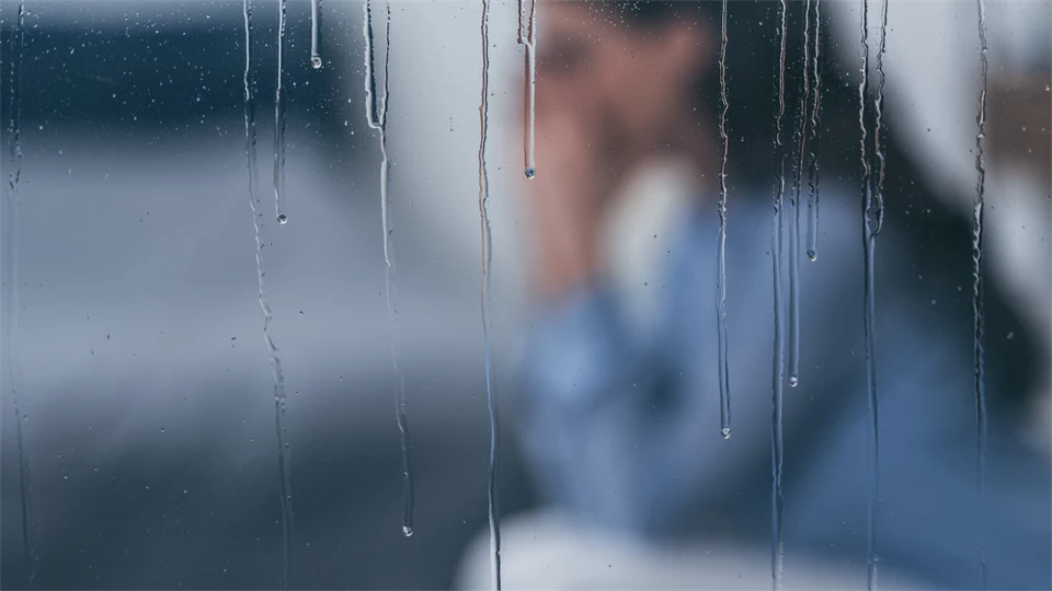 Selective focus of raindrops on windows with sad woman