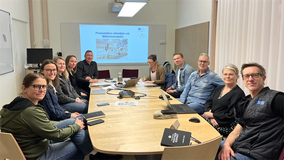 Tio personer sitter runt ett bord i ett mötesrum.