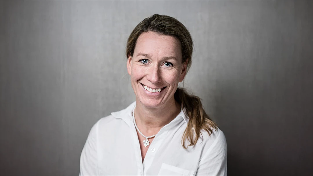 Kvinna med mörkt långt hår i hästsvans och klädd i vit skjorta.