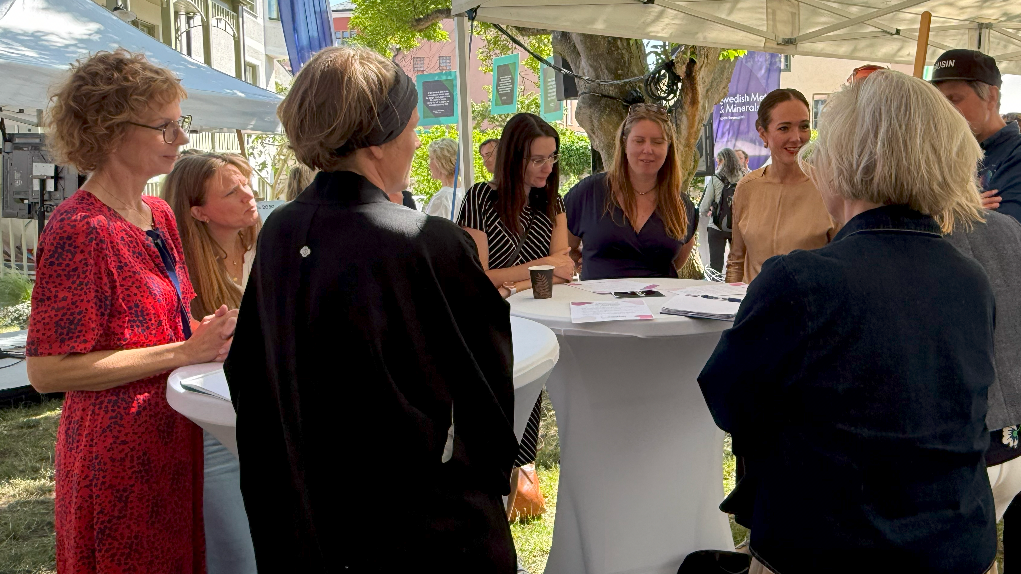 En grupp människor kring ståbord i en trädgård