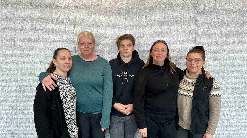 Fyra kvinnor och en man fotograferade framför en grå bakgrnd