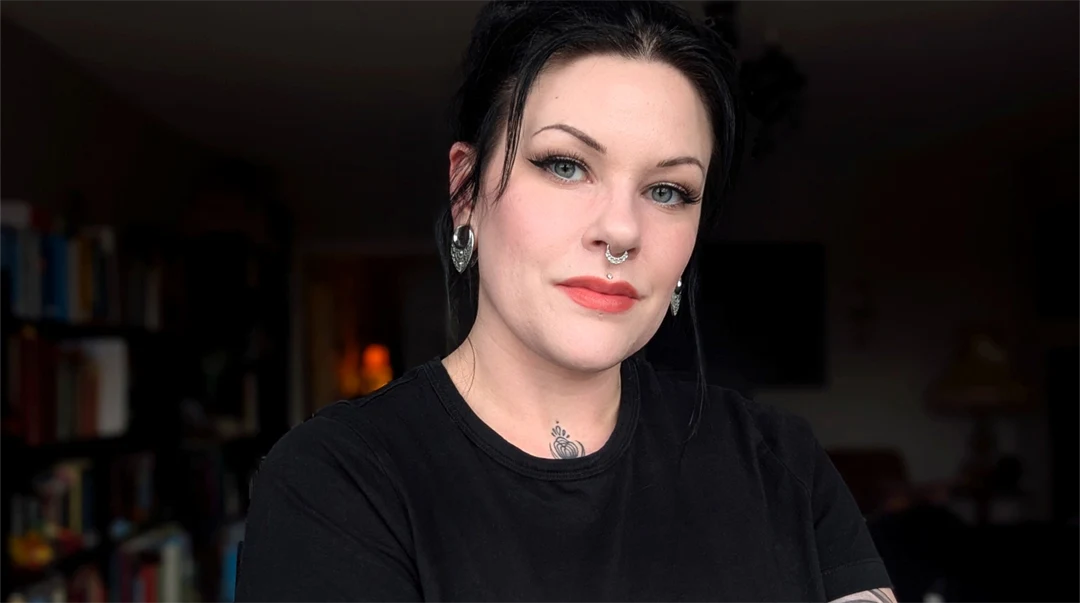 Porträtt av en kvinna i ett mörkt rum. Svart hår och rödmålade läppar, svart t-shirt 