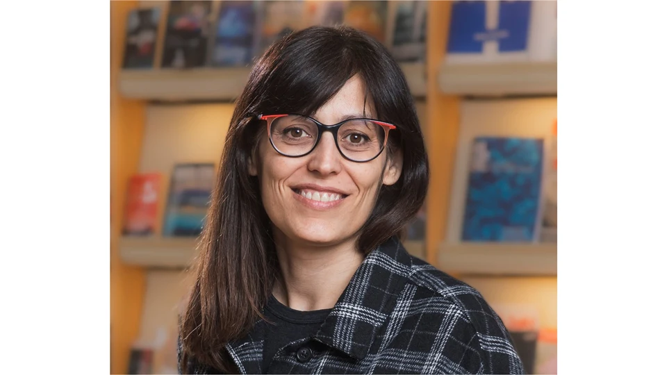 A woman with dark long hair, glasses and wearing a plaid shirt.
