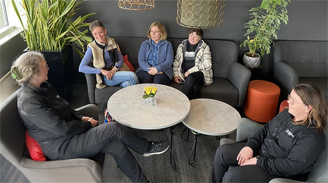 Fem personer sitter i soffgrupp och pratar.