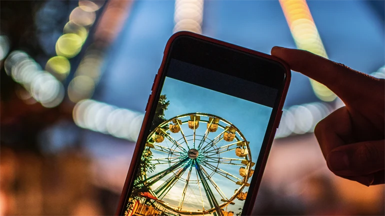 Metabild: Person tar en bild på ett Pariserhjul med mobilen och ser motivet både i mobilen och i verkligheten