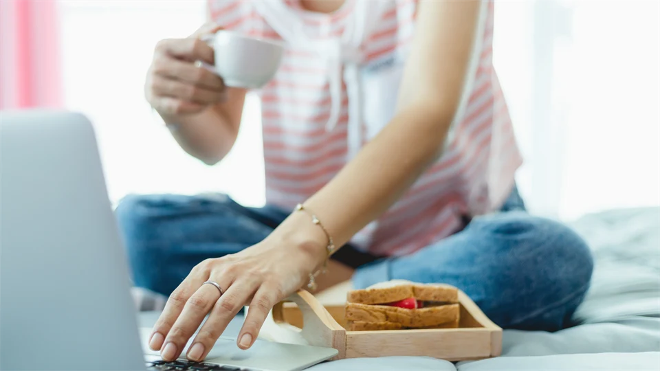 En person sitter och äter frukost i sängen med sin dator
