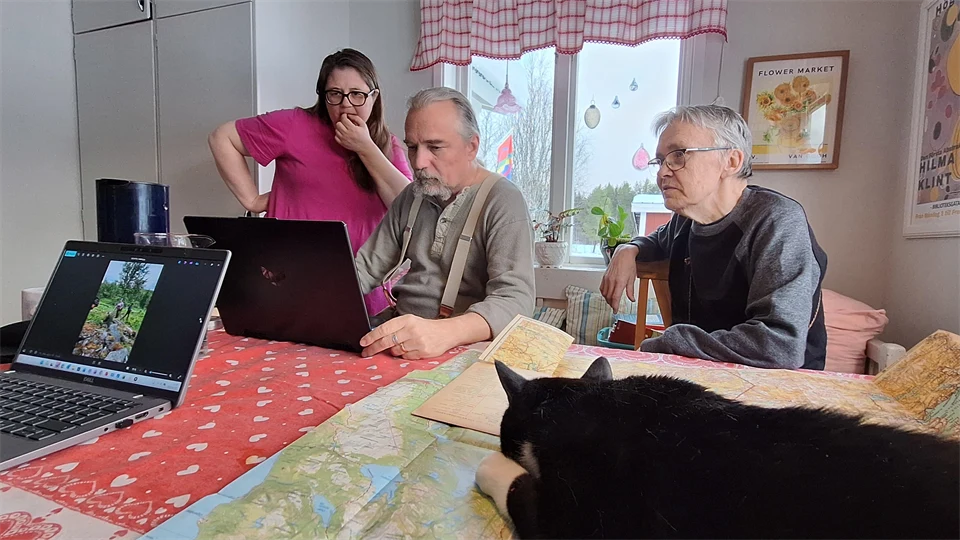 Tre personer arbetar vid ett köksbord. En katt ligger på en karta.