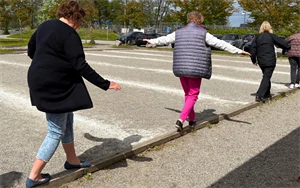 Kvinnor balanserar på en smal bräda vid en grusplan