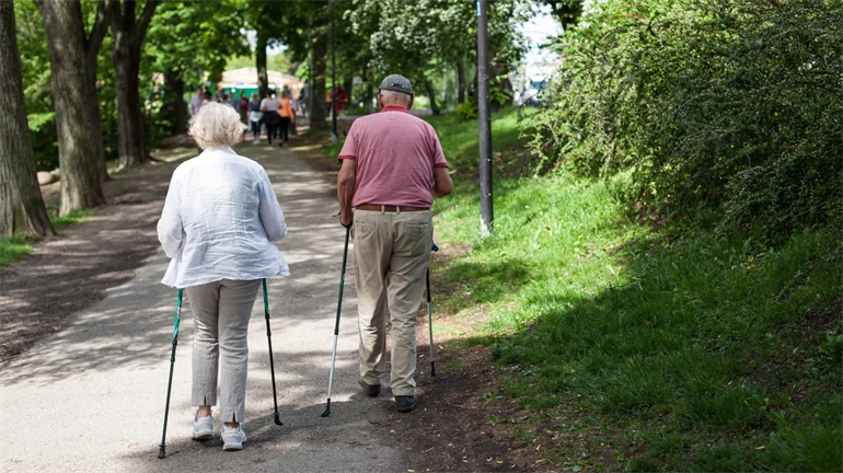 Äldre par går stavgång i parkmiljö.