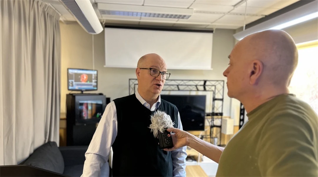 A man with a green shirt is interviewing a man with a navy shirt