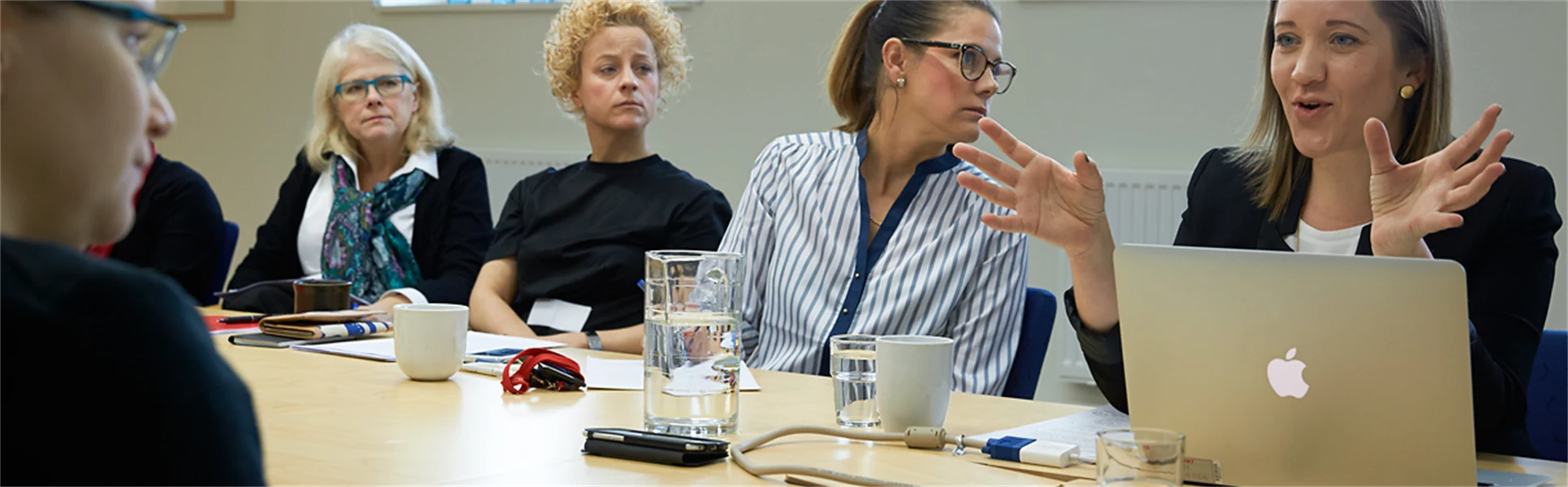 Fem kvinnor sitter vid ett konferensbord och diskuterar.
