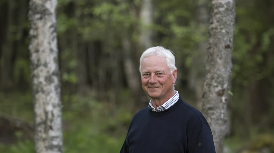 A man in a dark shirt stands in a forest.