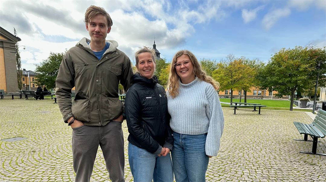 Tre personer stående på ett torg.