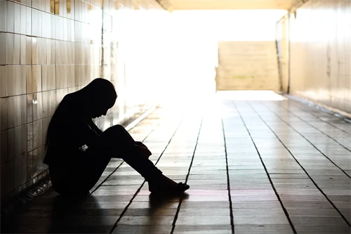 Siluetten av en tonåring som sitter lutad mot väggen i en gångtunnel och ser nedstämd ut.