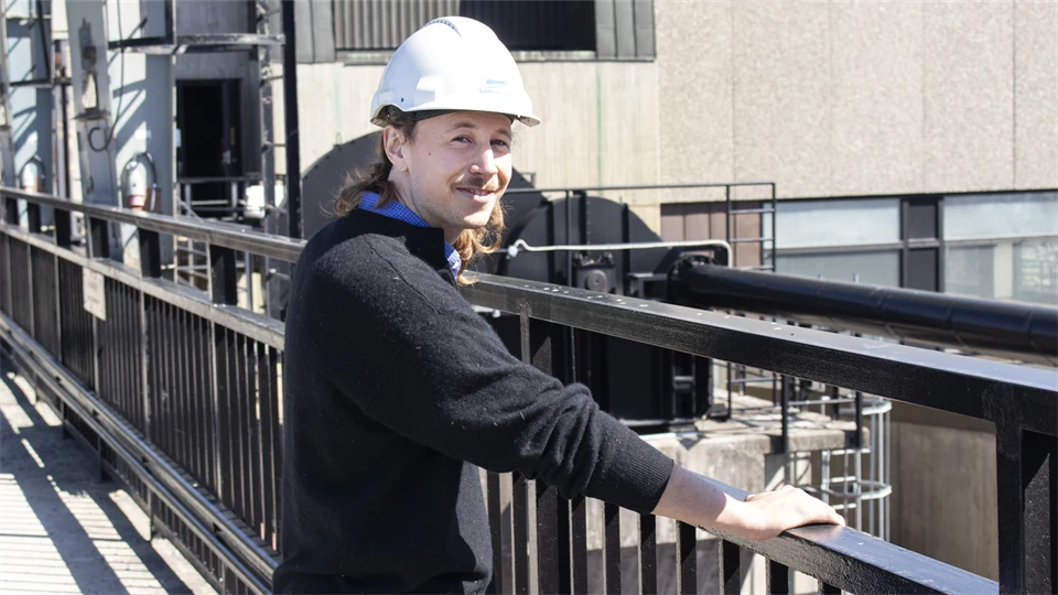  A man in a white helmet stands by a black fence in an industrial setting.
