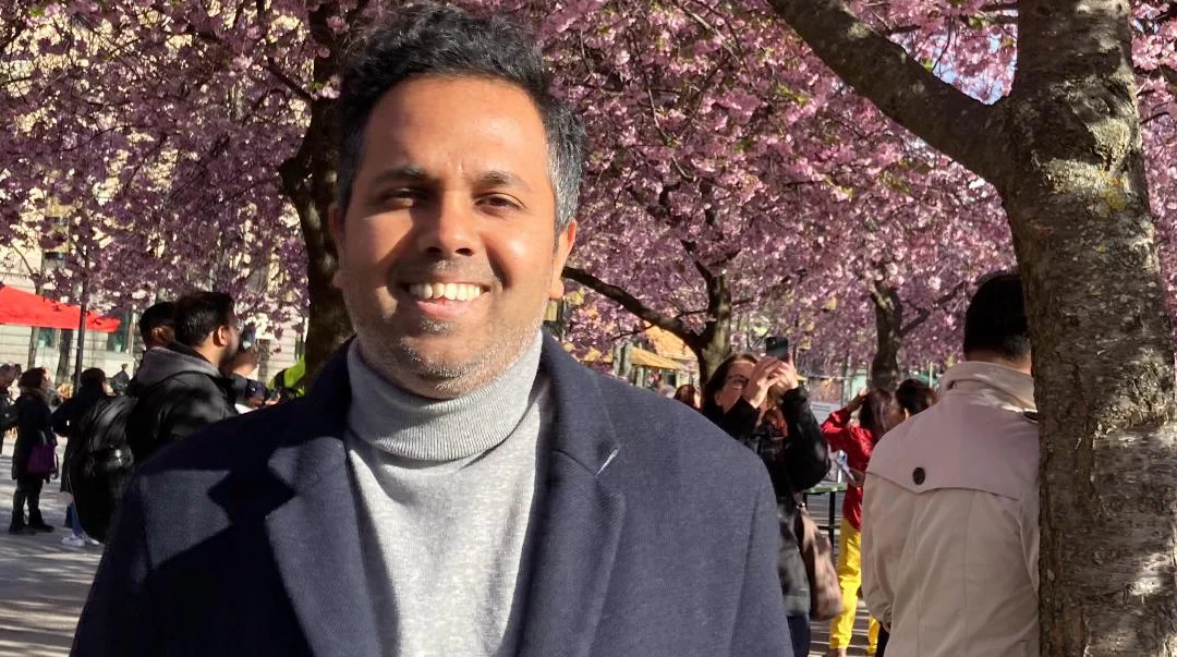 Man in a park surrounded by flowering trees and with people in the background.