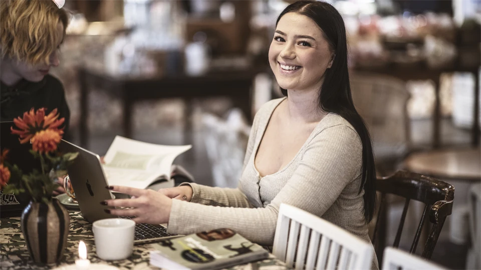 A woman is smiling at the camera. She is sitting by a computer.