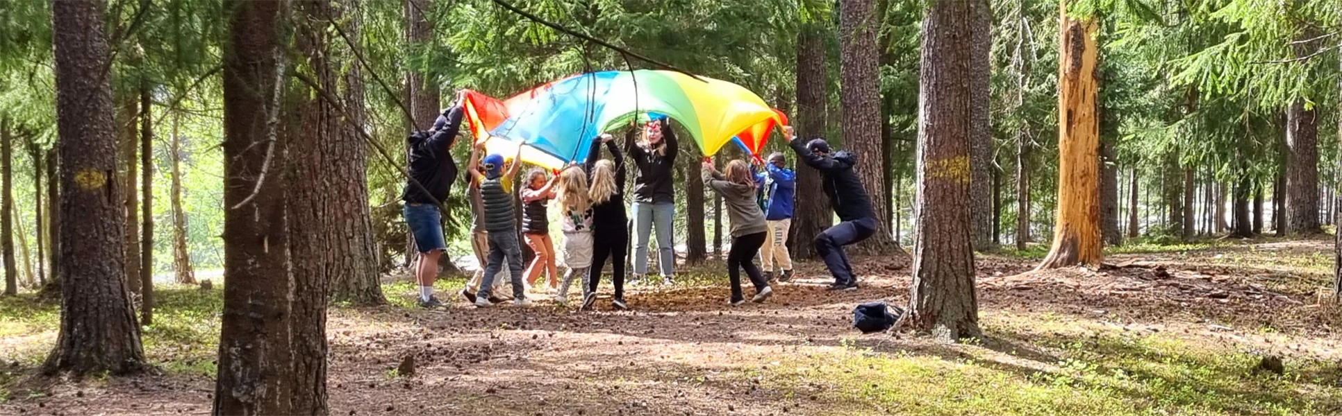 flera barn som håller upp ett färgglatt segel i skogen
