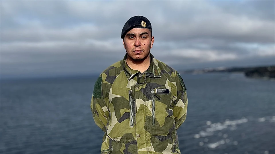 En man i militärkläder står på en klippa med havet i bakgrunden