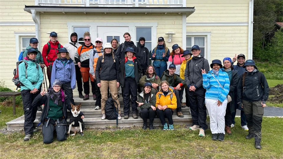 A group of people in outerwear standing in front of a yellow house