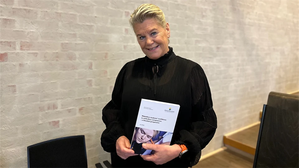 Kvinna klädd i svart håller upp en avhandling