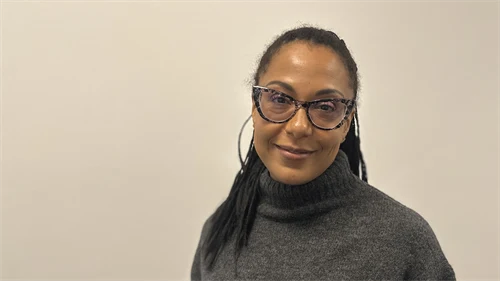 En kvinna i mörkt, uppsatt hår, glasögon och mörkgrå polotröja.