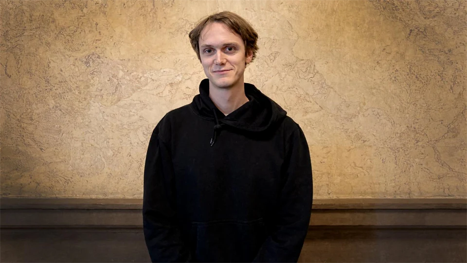 Man i svart hoodie står vid en vägg.