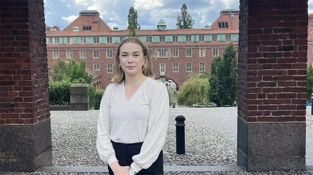 En kvinna med vit tröja och svarta byxor framför en byggnad